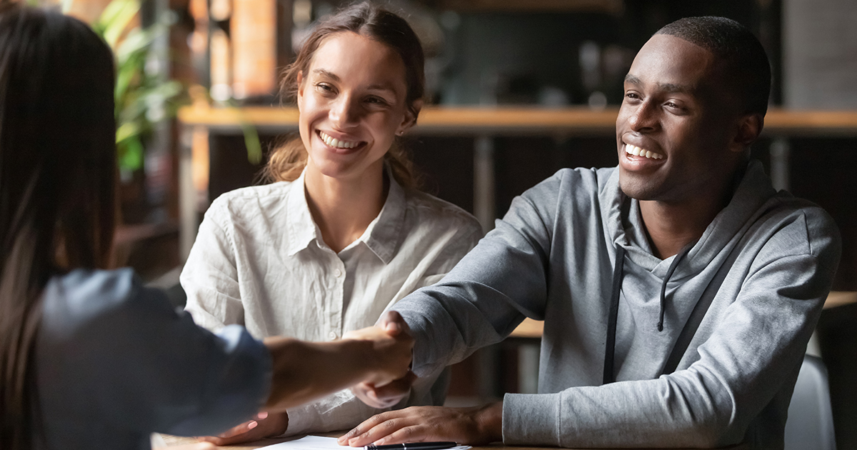 Young mixed race couple shaking hands with a woman across a table