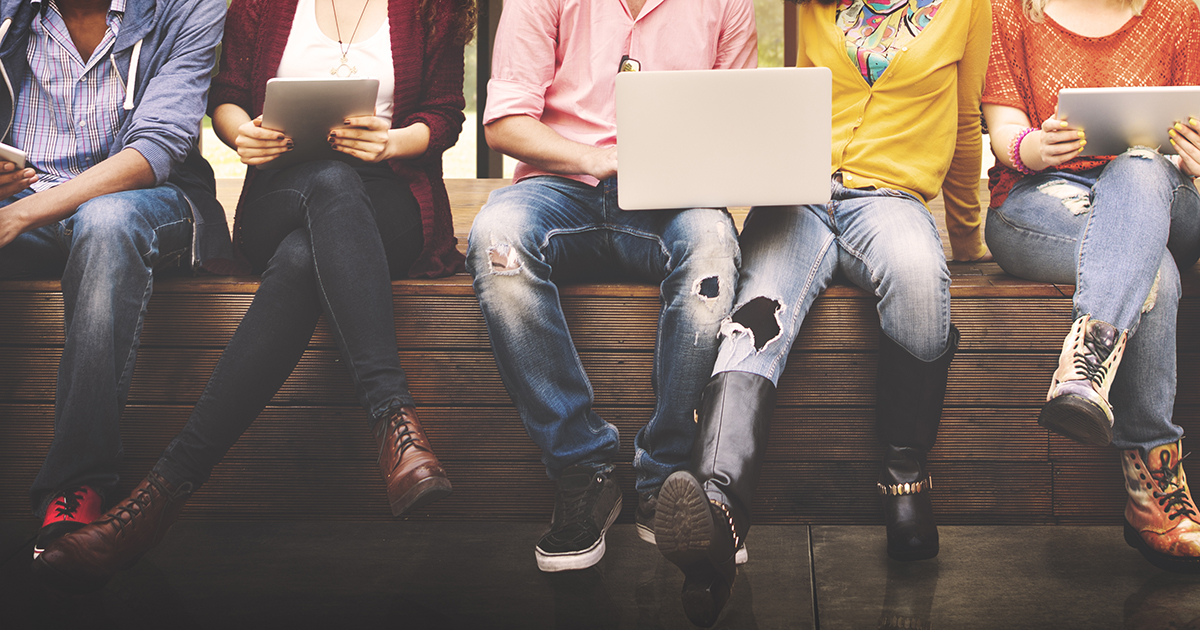 Group of young adults sitting in a row using laptops