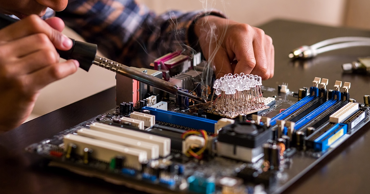 Hands working on a circuit board with tools