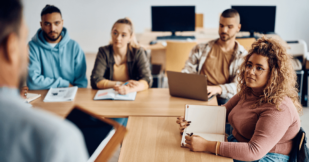 Diverse group of college students sitting at a table focus on an instructor in the foreground