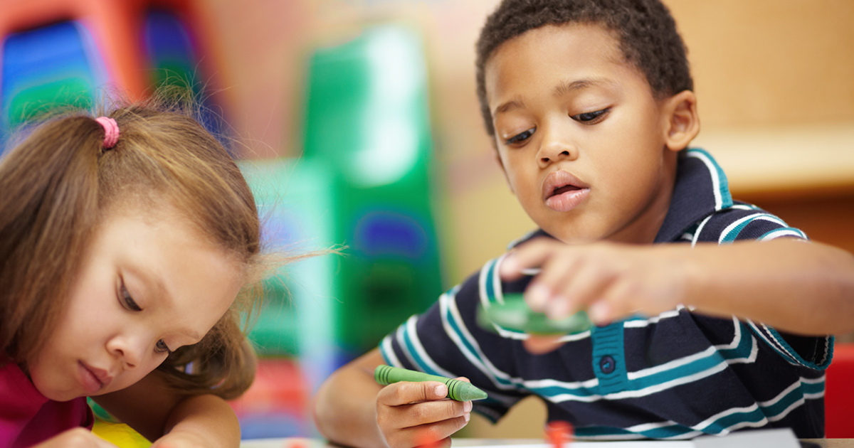 Two preschool-aged children play with crayons