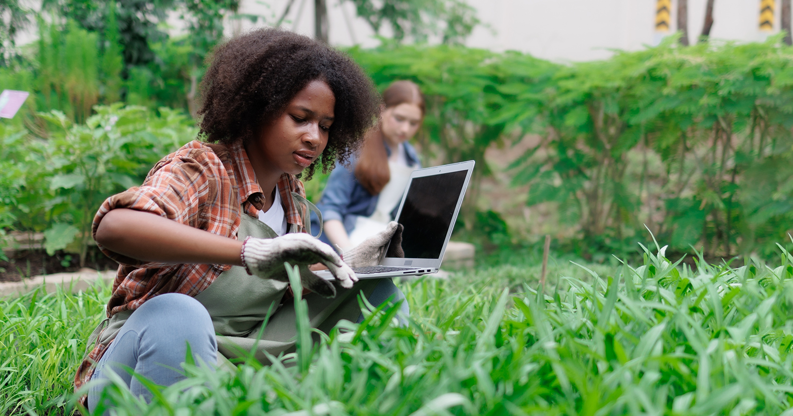 Two high school students in a garden, checking information on a laptop