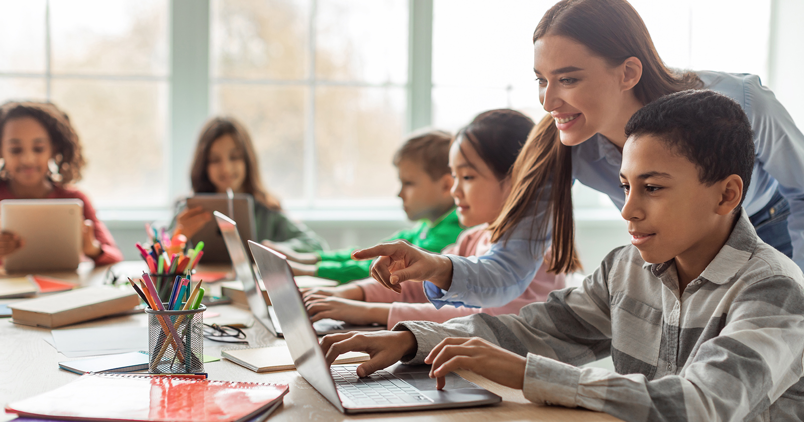 Teacher assists elementary school students as they use computers to learn