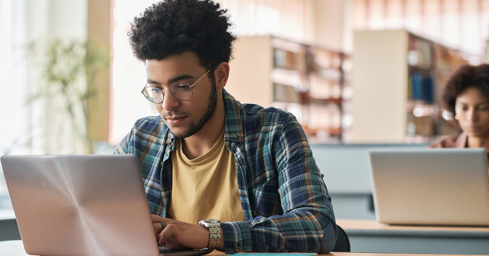 Male college student with glasses using a laptop in the library