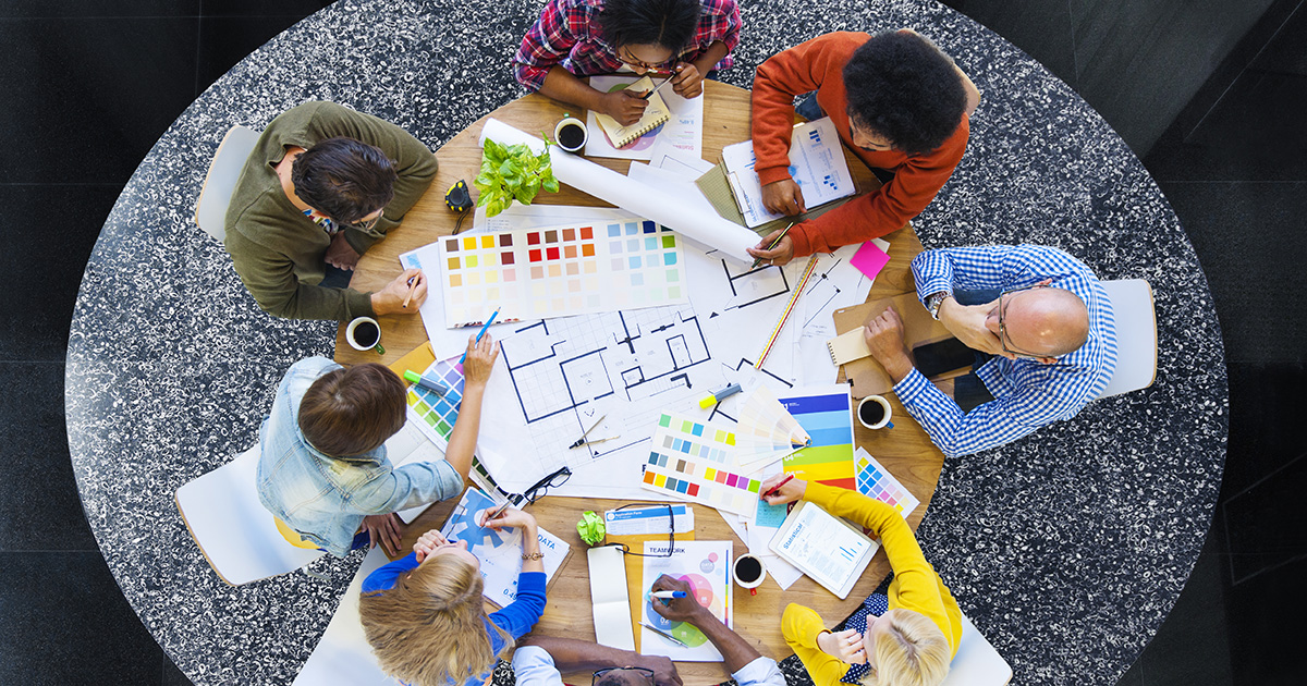 a group of coworkers sitting at a round table, shown from overhead, collaborating on a project 