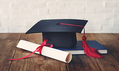 Graduation cap, diploma, a book resting on desk