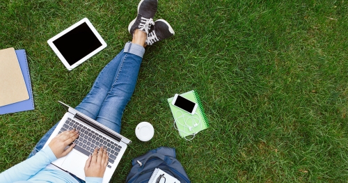 Student studying in a park, surrounded by books and mobile devices