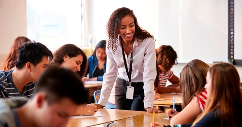 High school teacher leaning over a desk and speaking to students