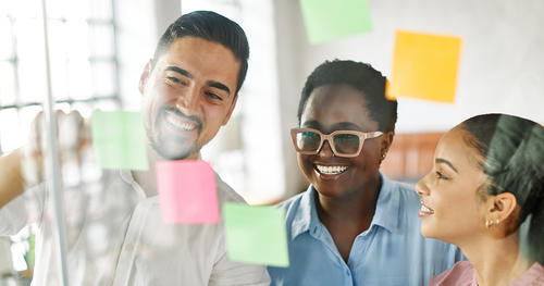 three people putting ideas on sticky notes