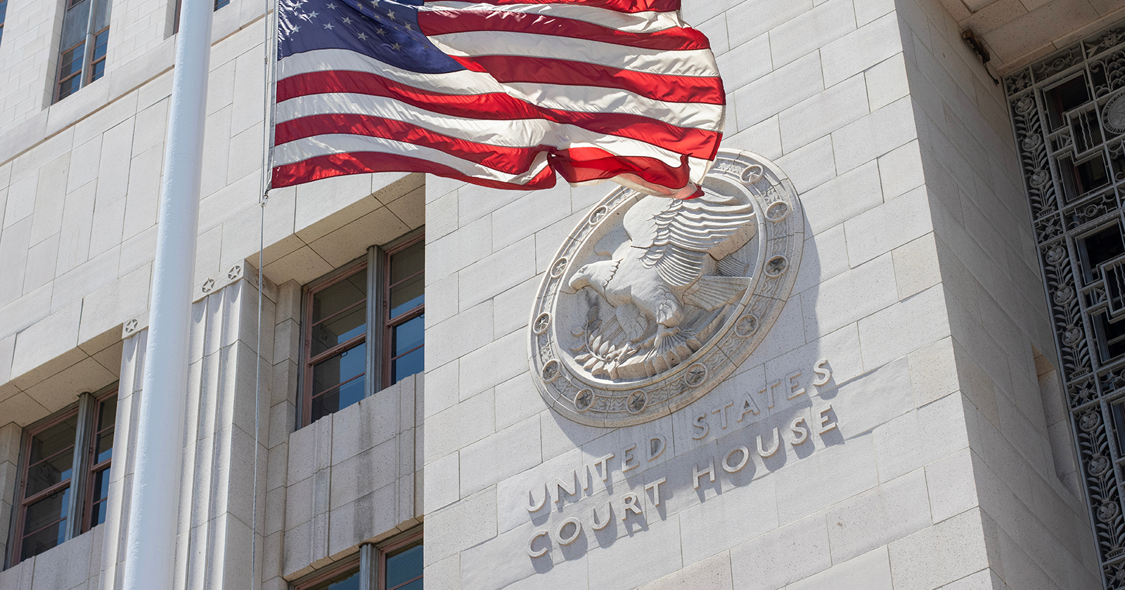 American flag waving in front of a building with a plaque that reads United States Court House