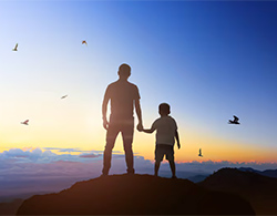 A father and son hold hands on top of a hill at sunset