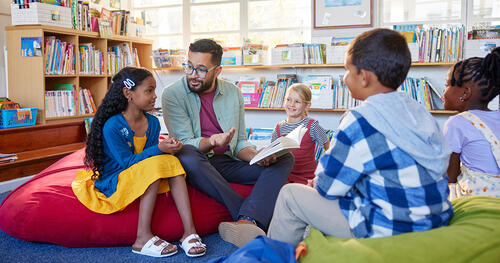 a male teacher is sitting on a floor in circle with kids