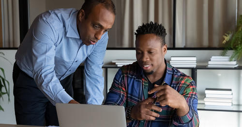 Mentor points to something on a computer screen as young Black intern looks