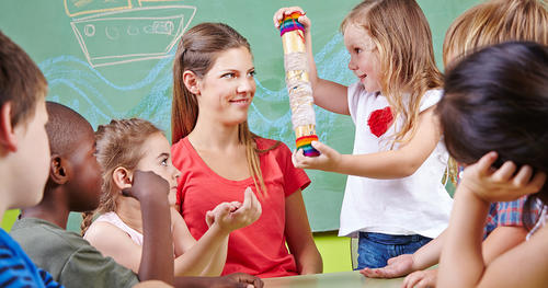 a treacher sittting among kids standing around her